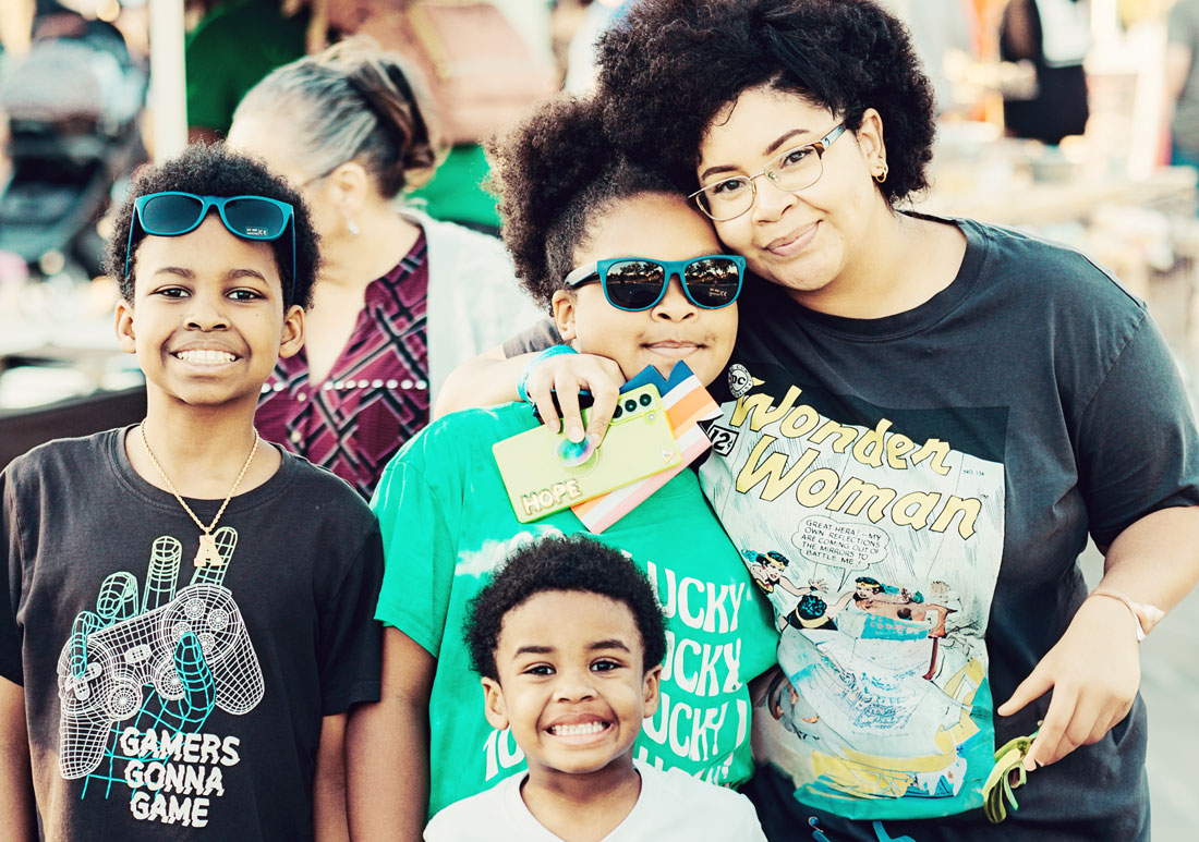 Mother with three children, embracing the one nearest to her as they all smile at camera