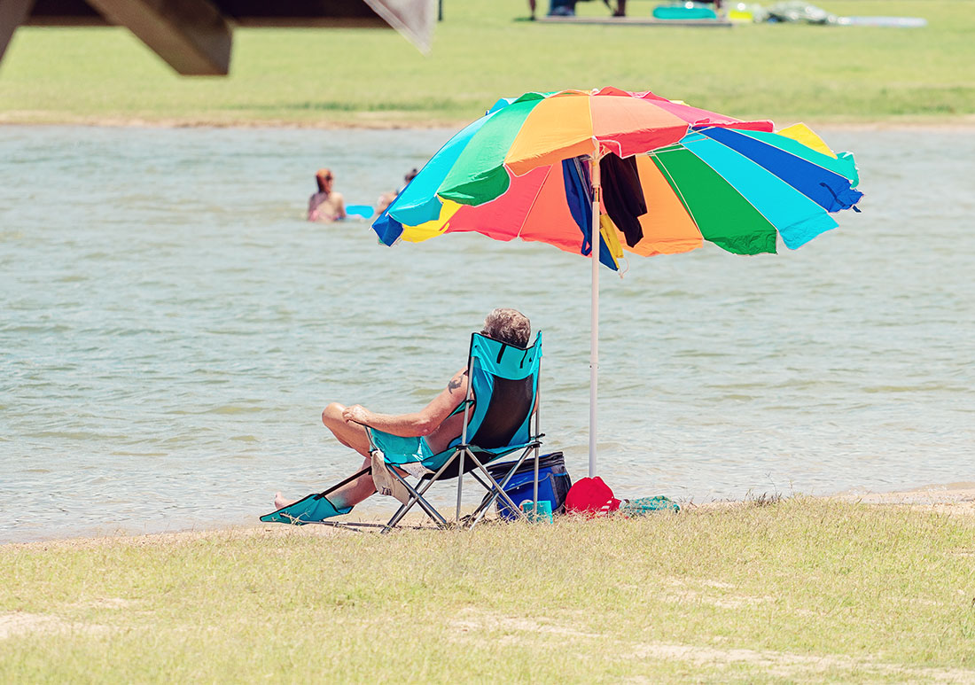 Man lounging in lawn chair under a shade umbrella next to a body of water