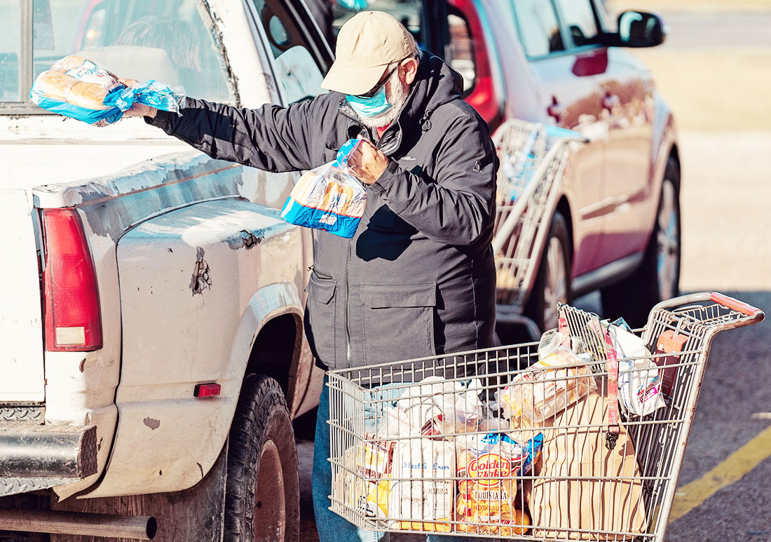 Man loading a truck with bread next to a shopping cart full of food