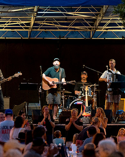 Band with various instruments perform in front of a multi-aged crowd