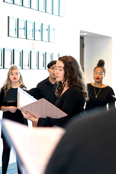 A young girl sings while looking at her song book, surrounded by her singing peers