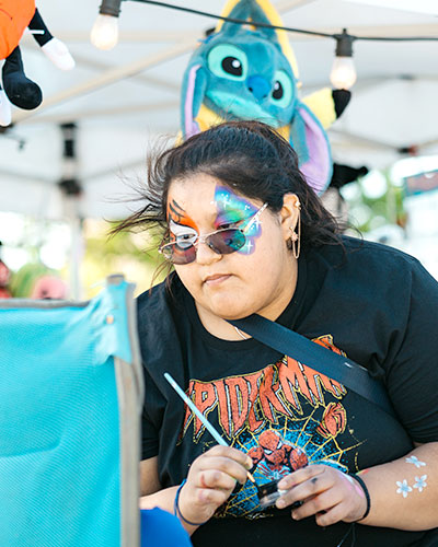 Woman with face paint looking at a person in a chair getting ready to paint their face