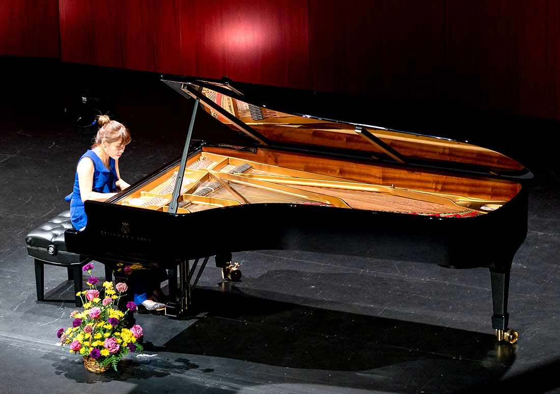 A woman playing the piano on a stage with a bouquet flowers at her feet