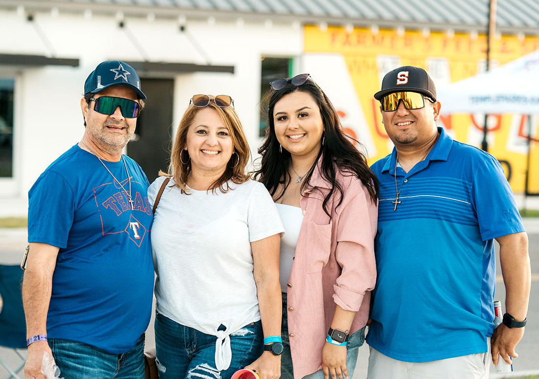 A family of four stand side by side and smile at the camera in a family portrait