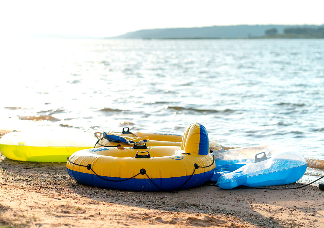 A collection of recreational water floatation devices next to a lake during late afternoon