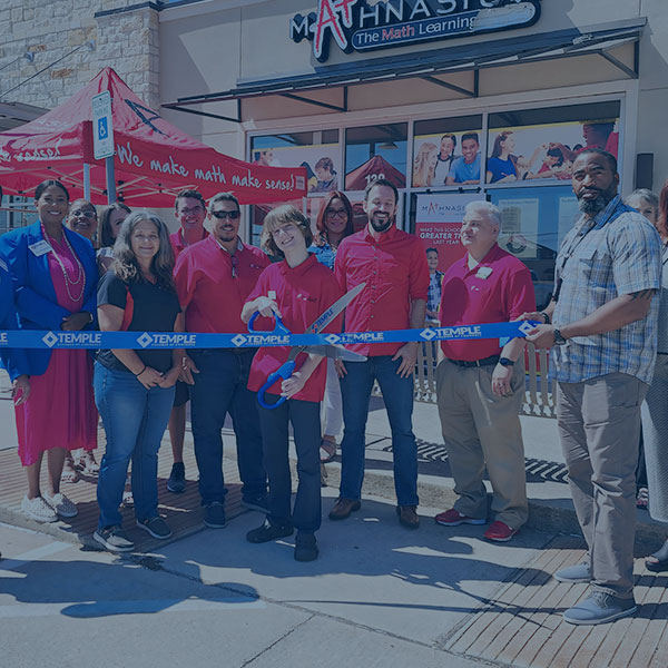 Group of people standing behind a "grand opening" ribbon holding a scissor about to cut the ribbon in front of a Mathnasium storefront