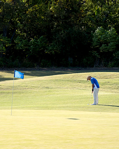 Man on the green of a golf course, preparing to putt a ball into the hole