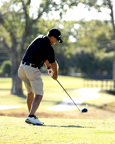 Man on a green golf course hitting a ball mid swing