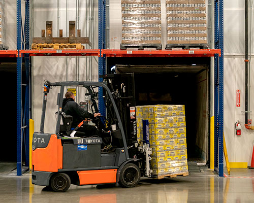 Man operating a small forklift lifting a stack of boxes