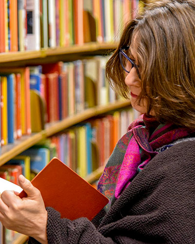 Close shot of a woman reading a book next to a row of books in a library