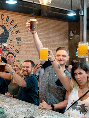 Patrons at a brewery raising a glass of beer hooting at the camera