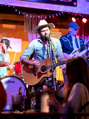 Man in a hipster cowboy hat playing acoustic guitar and singing supported by a band