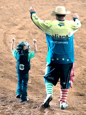 Child and rodeo clown walking together with arms raised.