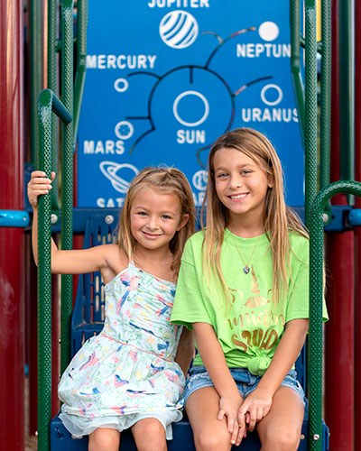 Two young girls sit in front of an interactive solar system installation