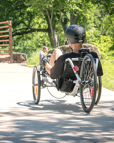 Man riding a reclining tricycle through a paved path in the woods