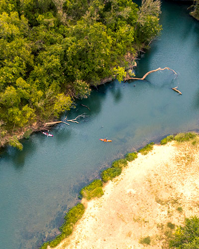 Drone shot of two kayakers on a river, one side of the river is dense forest