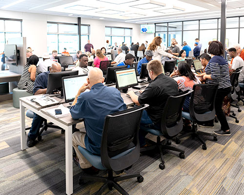 Group of people at computers at a workforce support facility with mentors aiding the users