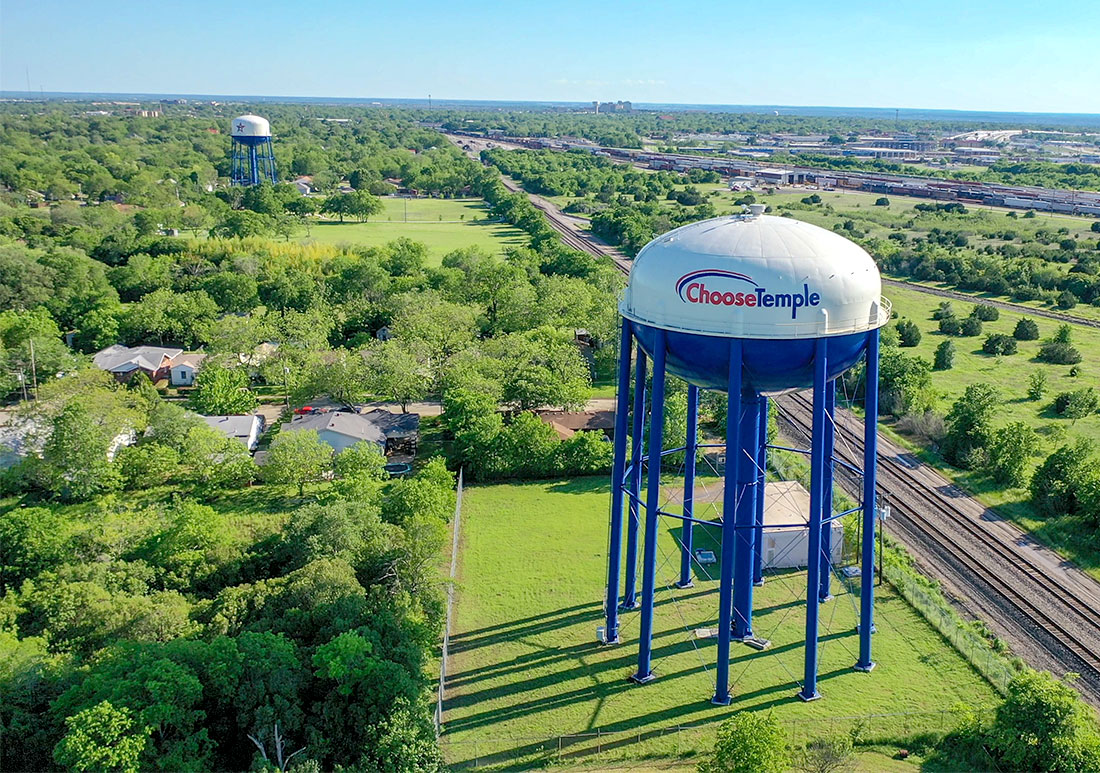 Aerial shot of a watertower with the words "Choose Temple" printed on it, surrounded by a neighborhood and train tracks