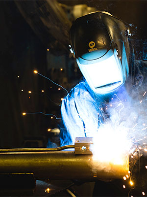 Man in welder's mask welding a metal pipe as sparks fly