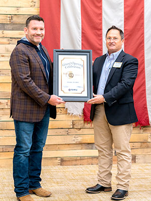 Two men in front of a large American flag holding a plaque